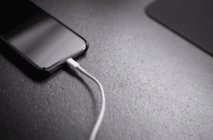 Black iPhone plugged into Lightning USB charging cable on black surface
