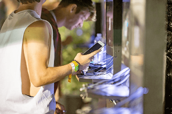 Close up of man using dead phone charging at Uber lounge during Coachella music festival